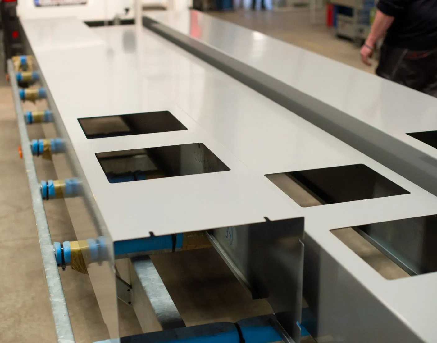 Plaques métalliques grises avec découpes carrées sur un support industriel, dans un environnement d'atelier.