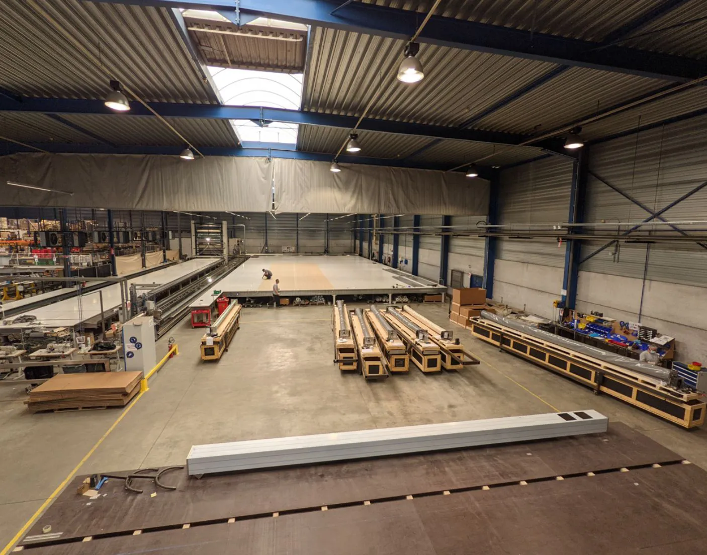 Intérieur d'une usine avec de grandes machines alignées sur le sol en béton, sous un toit en tôle ondulée avec éclairage suspendu.