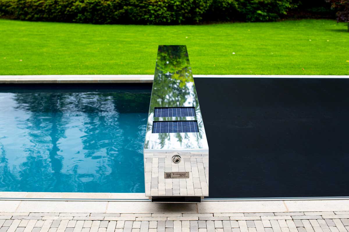 Une couverture de piscine avec un effet miroir et des panneaux solaires, entourée d'une pelouse verte et d'un carrelage beige.