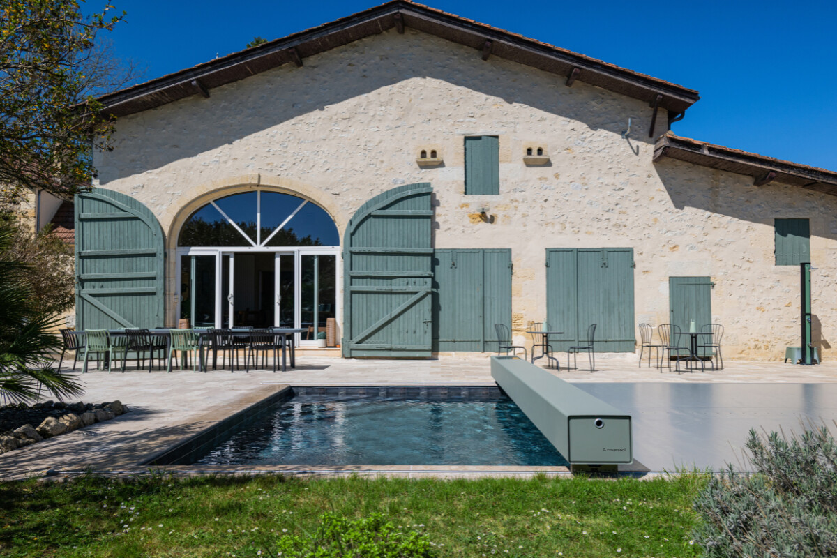 Gros plan sur l'habillage de la Coverseal grise au bord de la piscine, avec en arrière-plan les transats et la maison en pierre.