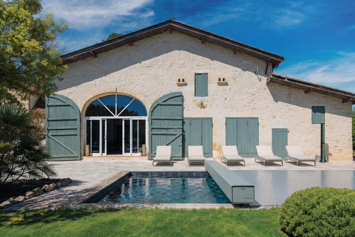 Gros plan sur l'habillage de la Coverseal grise au bord de la piscine, avec en arrière-plan les transats et la maison en pierre.